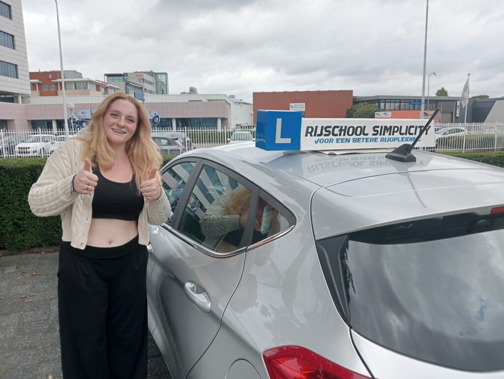 Rijlessen Eindhoven Eindhoven Een stralende jonge dame naast een lesauto, viert haar geslaagde praktijkexamen in Eindhoven.