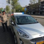 Rijlessen in Eindhovenjubilant man celebrating his driving test success next to his learner car.