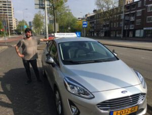 Rijlessen in Eindhovenjubilant man celebrating his driving test success next to his learner car.